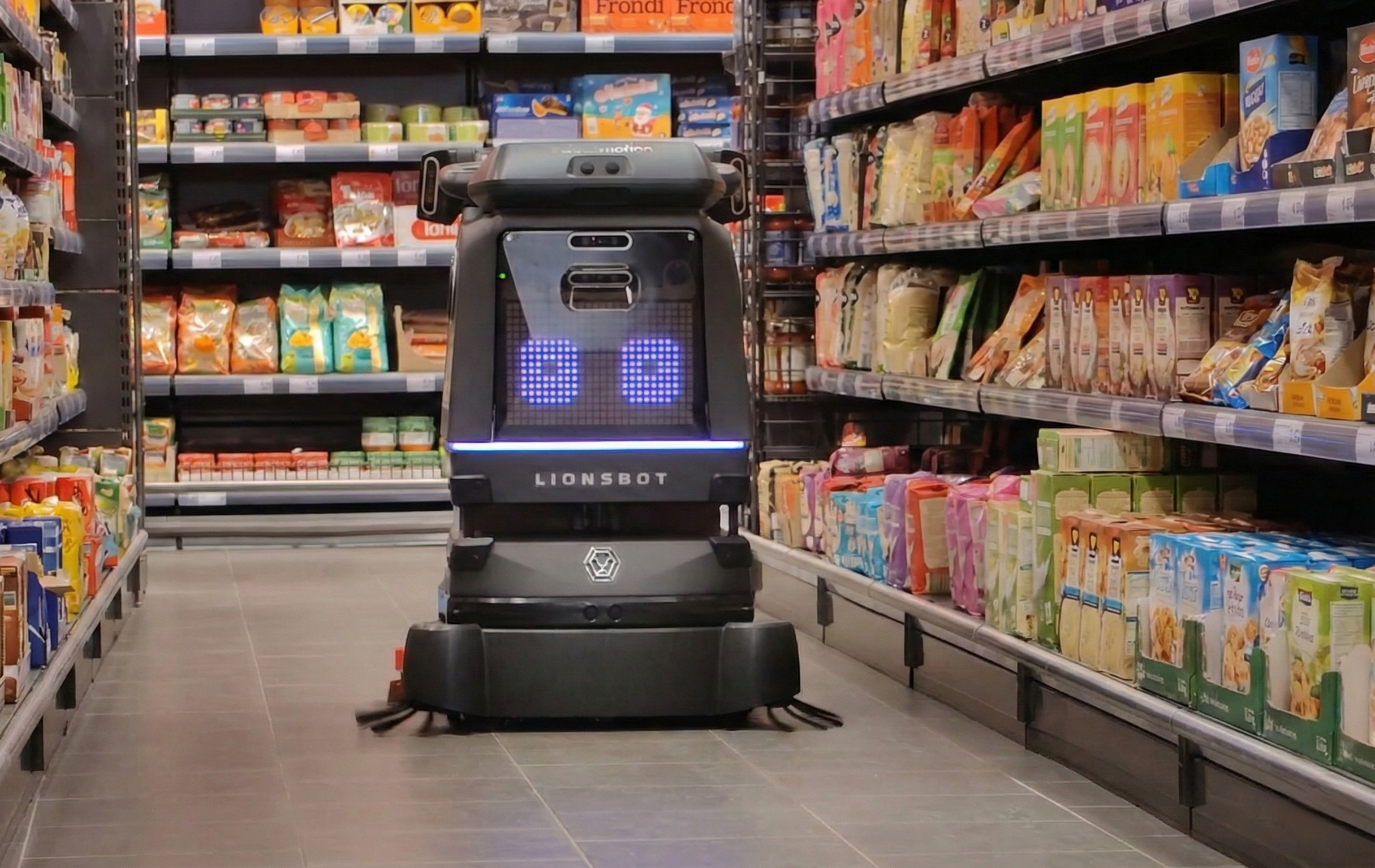Ein Reinigungsroboter von Salesmotion Robotics bewegt sich im Gang eines Lebensmittelgeschäfts zwischen den Regalen mit verpackten Lebensmitteln.